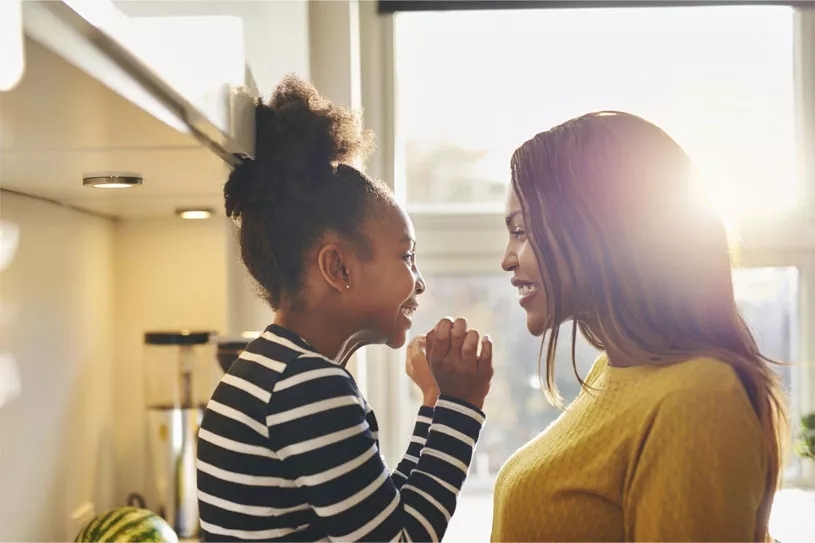 Mom playing with daughter in front of a sunlit window.