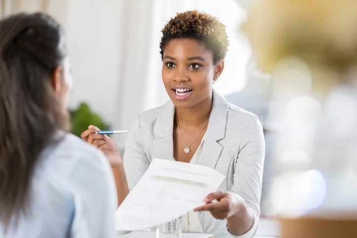 A woman presenting in a meeting with a pen and paper.